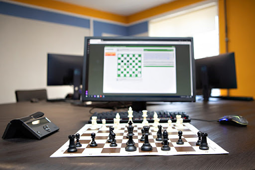 на картинке изображён монитор на экране которого электронное шахматное поле, а около монитора расположена шахматная доска с расставленными фигурами