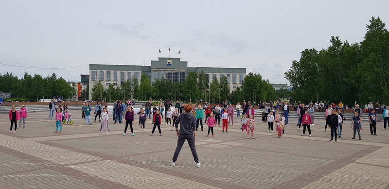 на фотографиях участники массовой фитнес зарядки, прошедшей на площади возле Сургутской филармонии в День города.