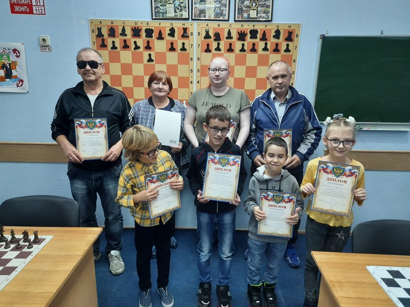 на фотографии участники соревнований по шахматам среди лиц с ограниченными возможностями здоровья в шахматно-шашечном клубе «Белая ладья» с дипломами: четверо взрослых и четыре ребенка